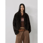 Woman wearing a dark brown fur coat over a patterned sweater with a plain background