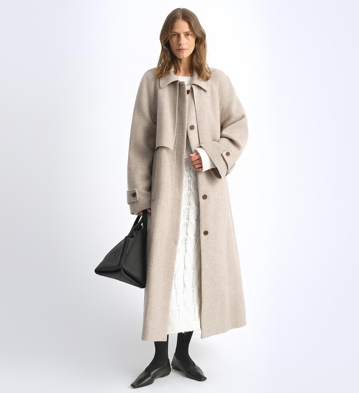 Woman wearing a long beige coat on a white background