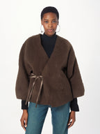 Woman wearing a brown wrap-style jacket with a white background