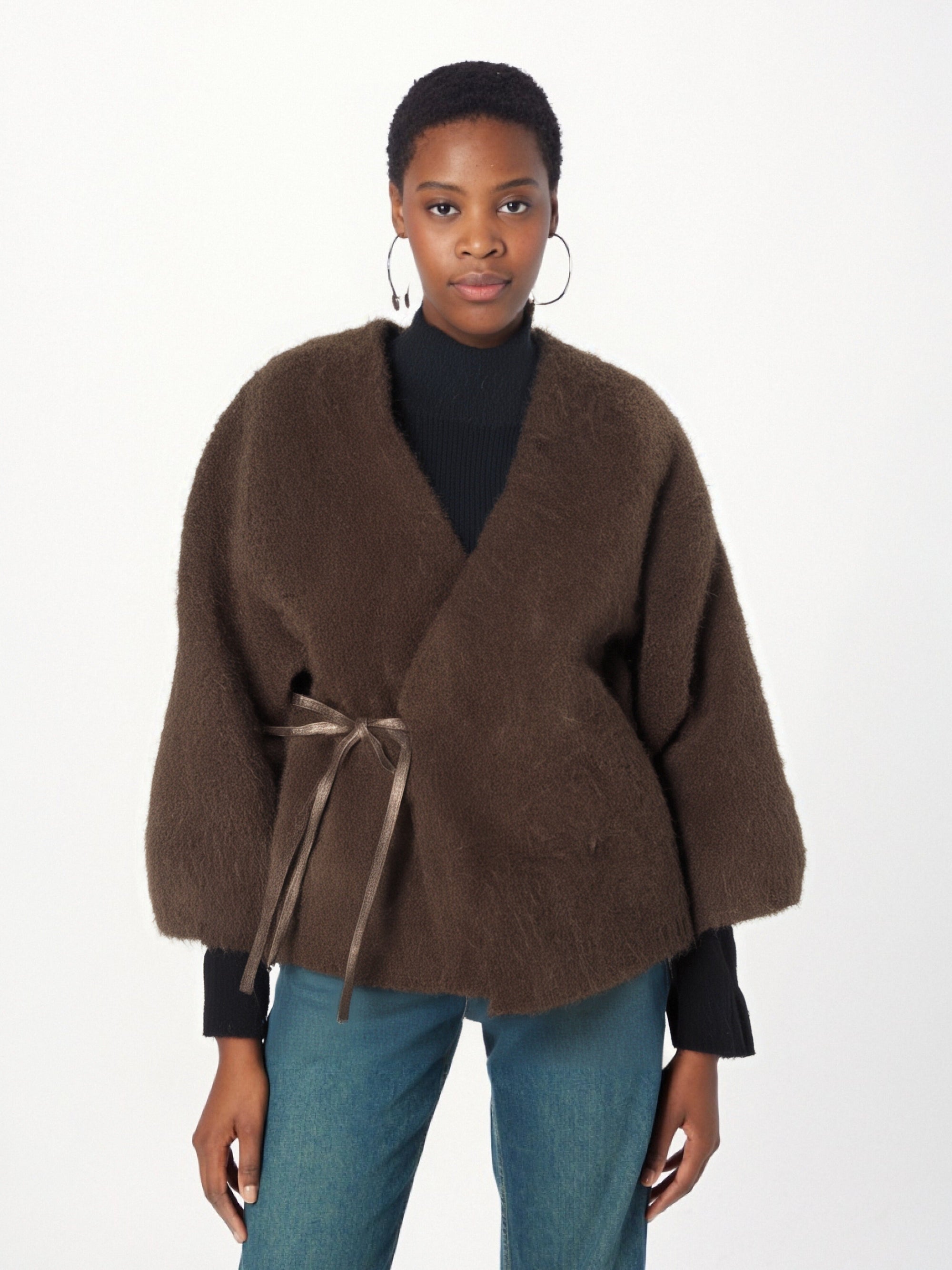 Woman wearing a brown wrap-style jacket with a white background