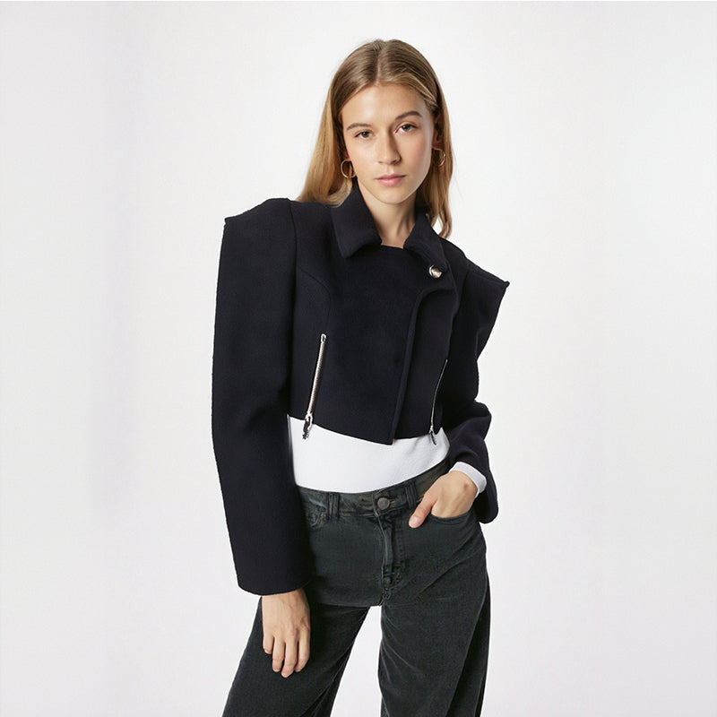 Woman wearing a black jacket with a white shirt and black pants on a light gray background