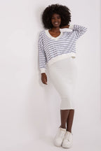 Woman wearing a striped sweater and white pants against a plain background