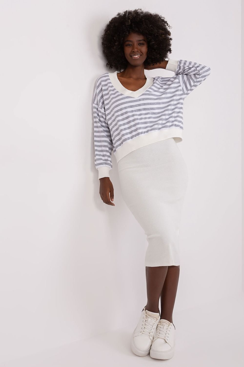 Woman wearing a striped sweater and white pants against a plain background