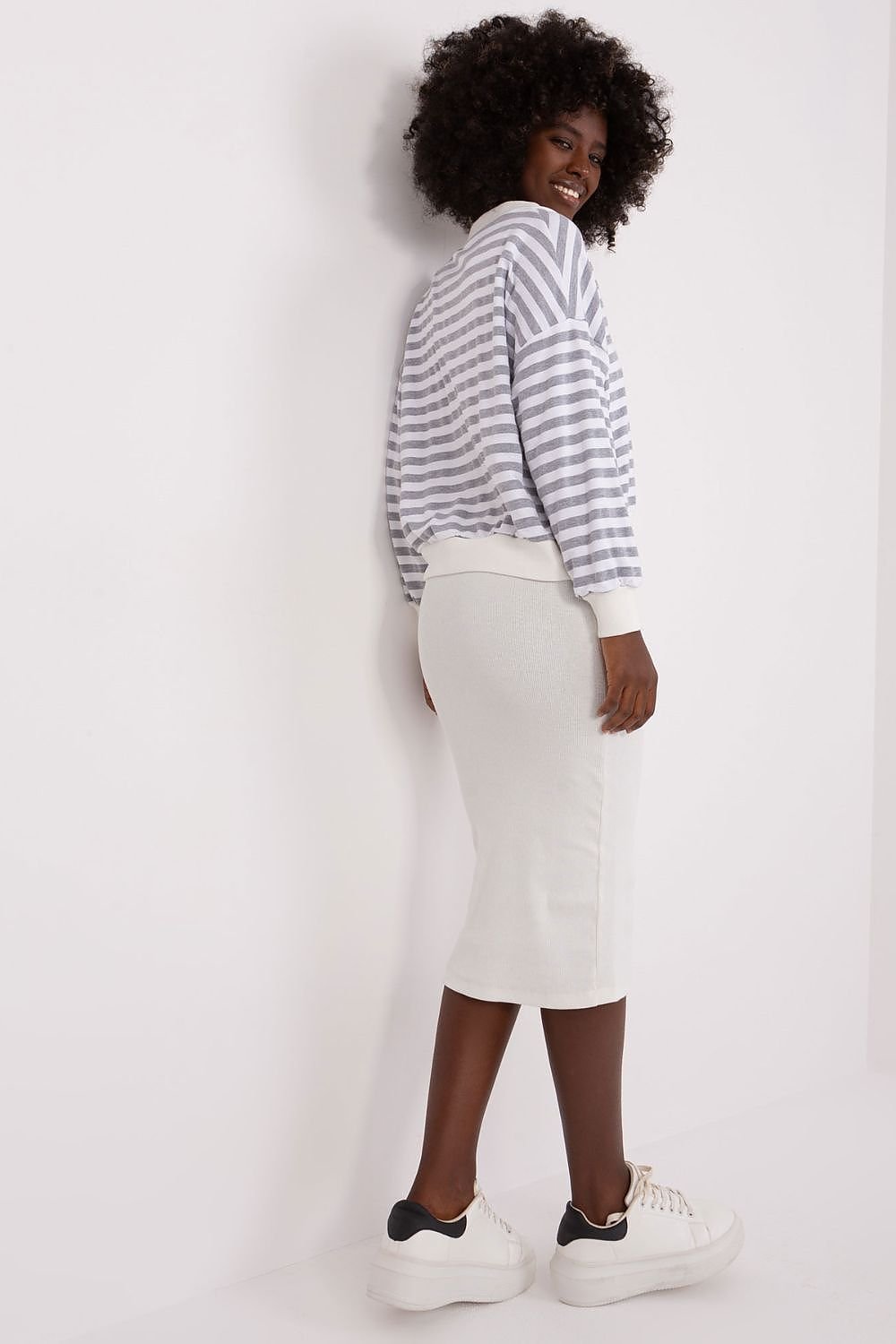 Person wearing a striped sweater and white pants against a plain background