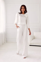 Woman wearing a white outfit with a flower detail in a minimalistic room.