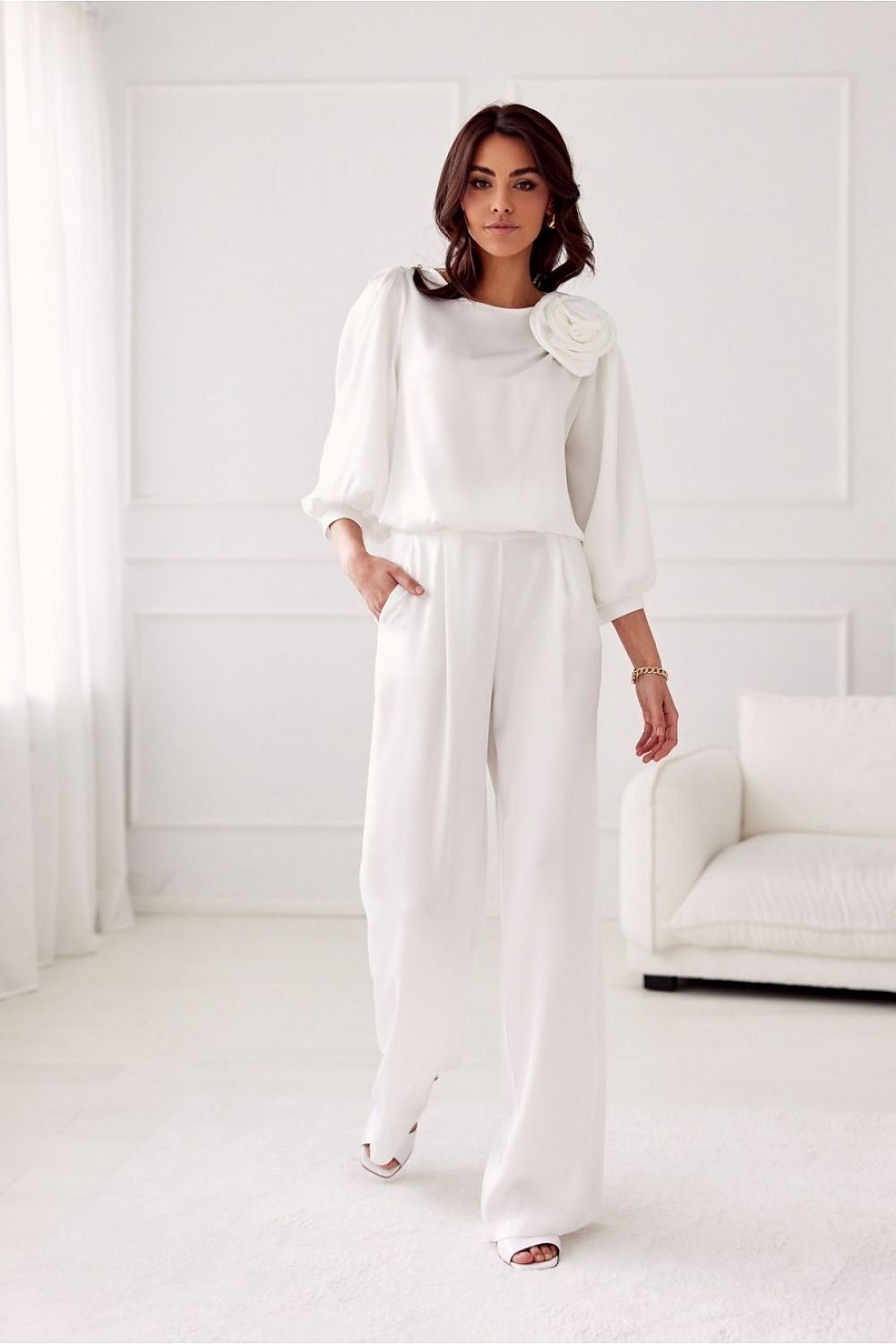 Woman wearing a white outfit with a flower detail in a minimalistic room.