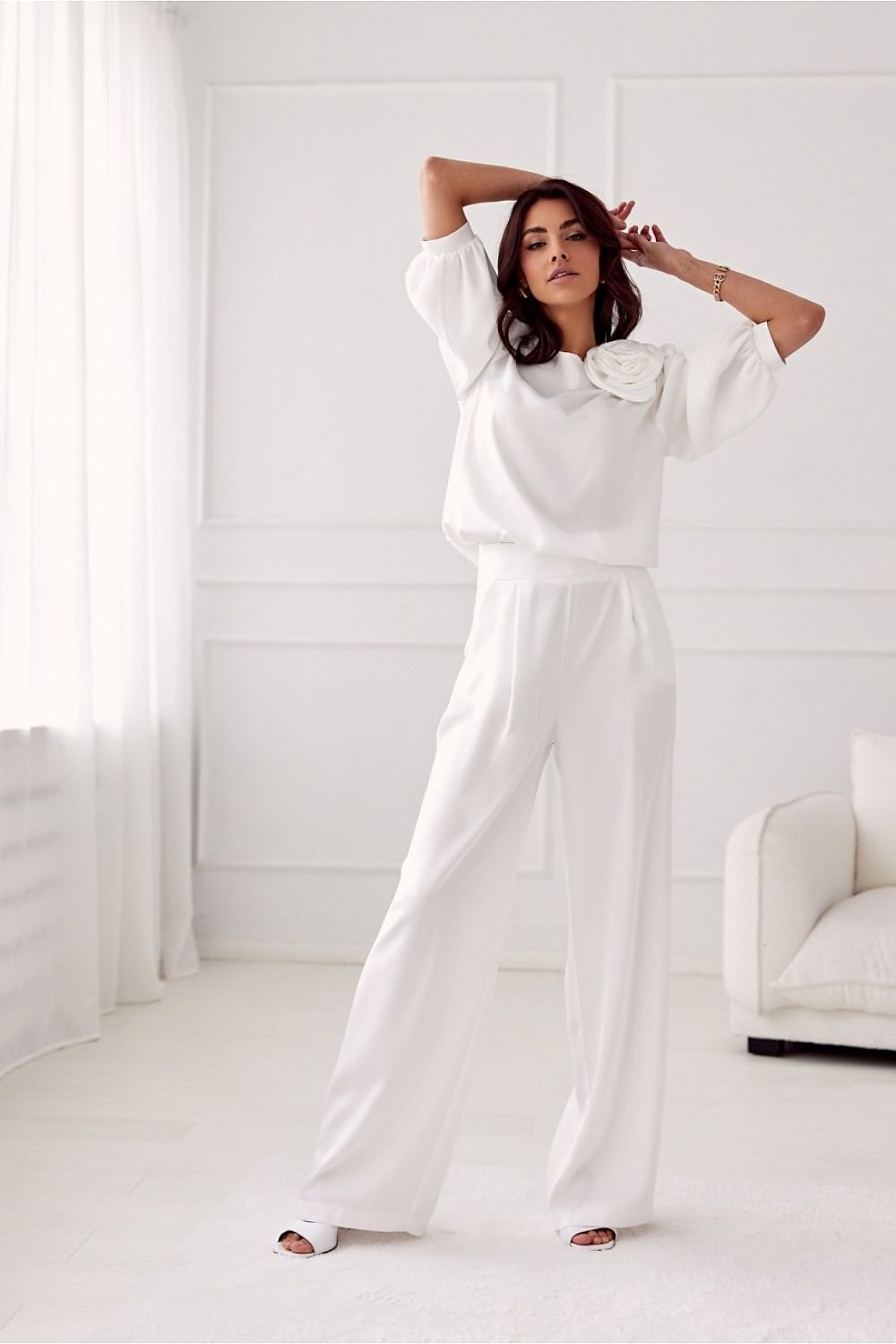 Woman in a white outfit standing in a bright, minimalistic room.