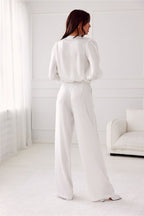 Woman in a white outfit standing in a minimalistic room with white walls and furniture.