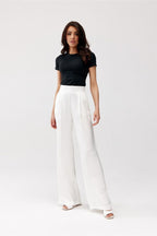 Woman wearing a black top and white pants on a white background