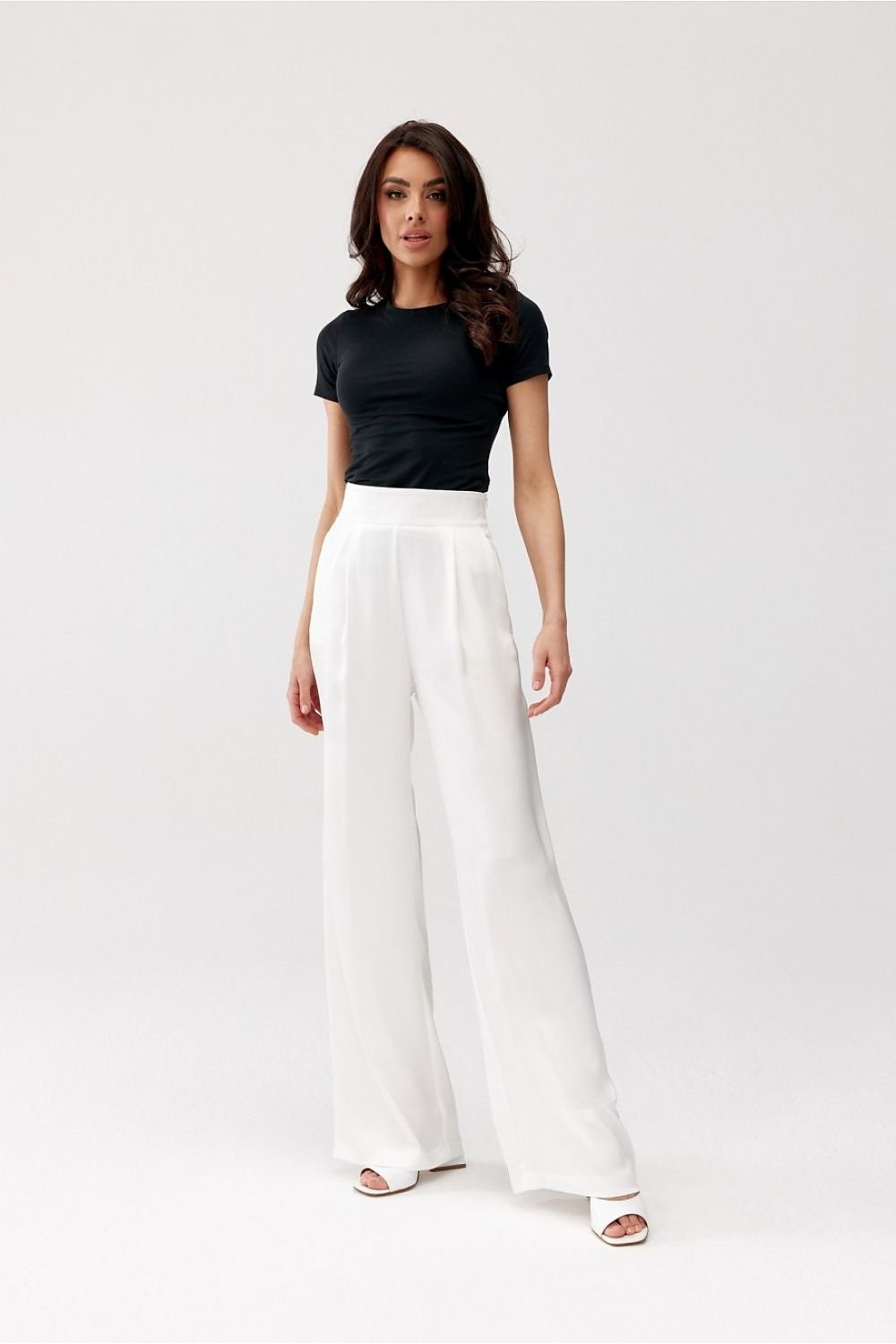 Woman wearing a black top and white pants on a white background