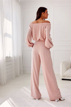 Woman wearing a pink off-shoulder top and wide-leg pants in a bright room.