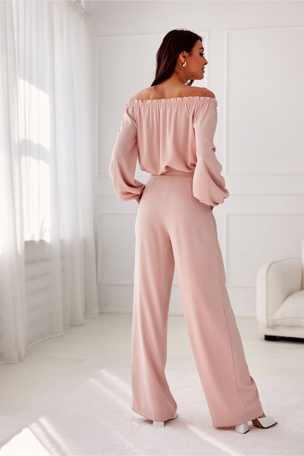 Woman wearing a pink off-shoulder top and wide-leg pants in a bright room.