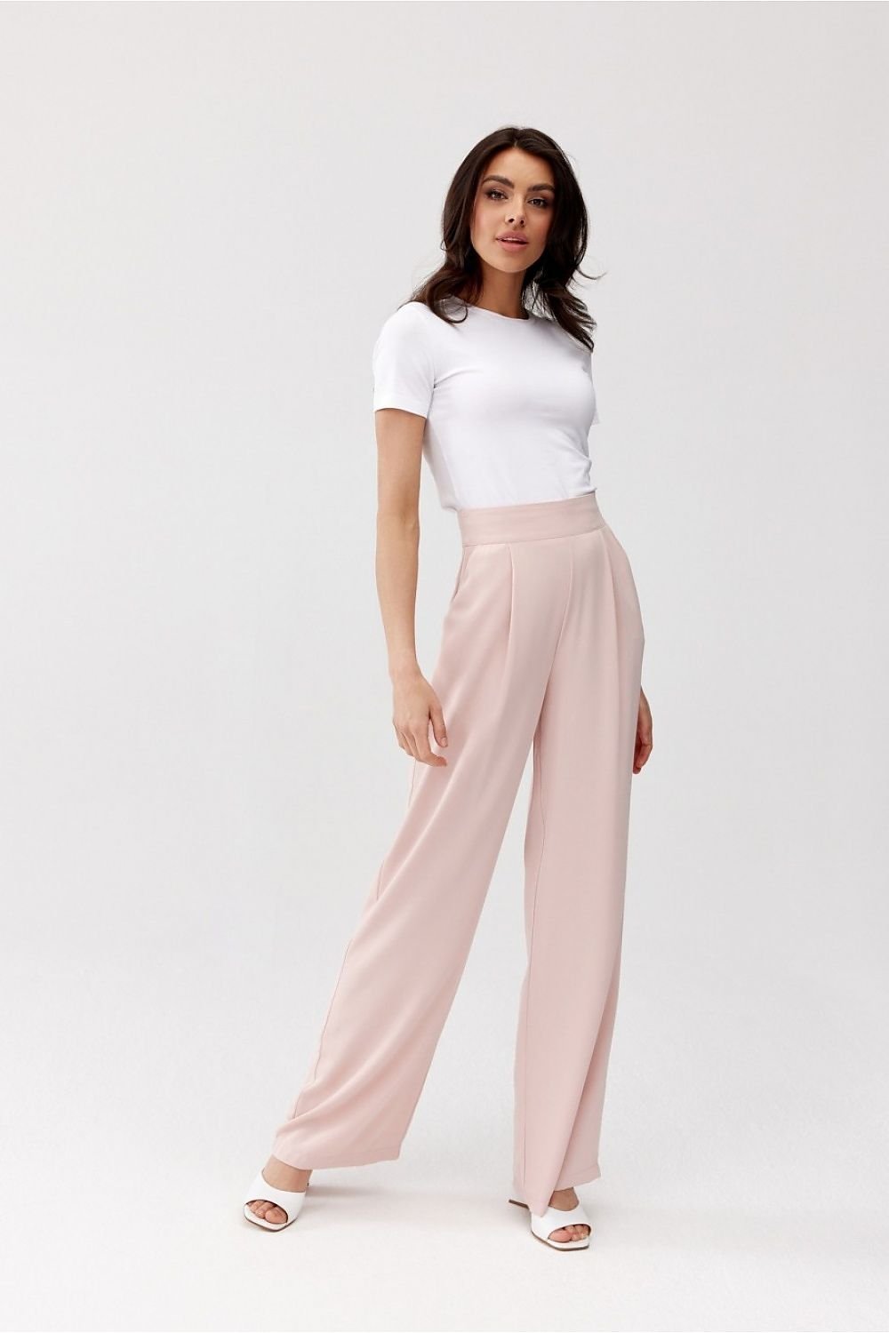 Woman wearing a white top and light pink pants on a white background