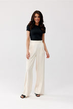 Woman wearing a black top and white pants on a white background