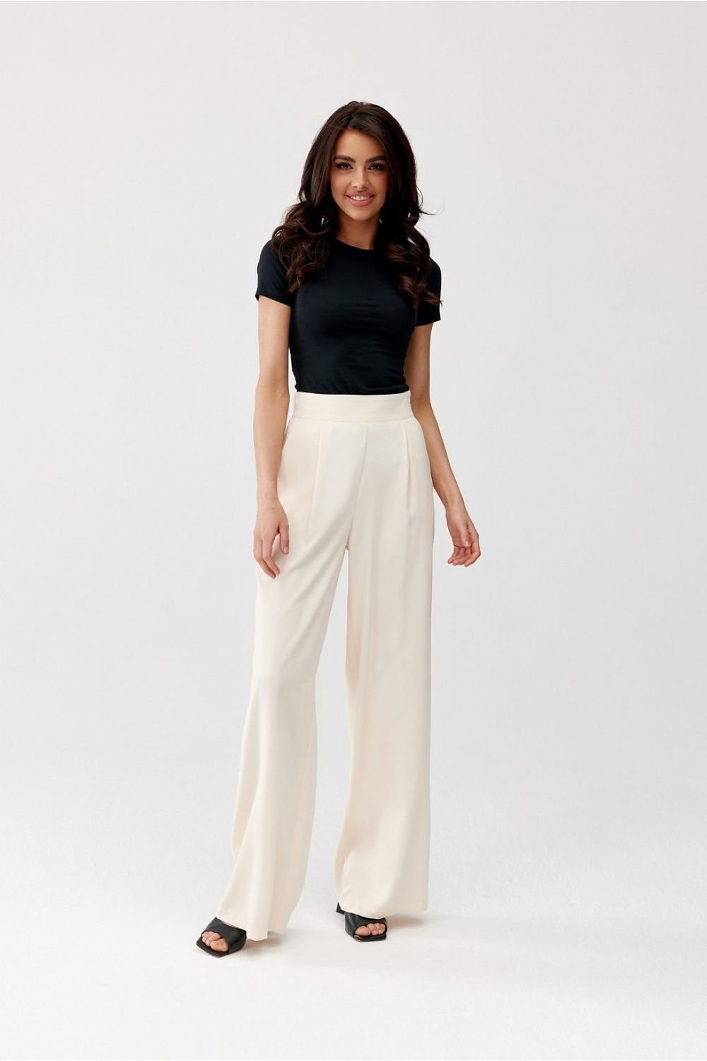 Woman wearing a black top and white pants on a white background