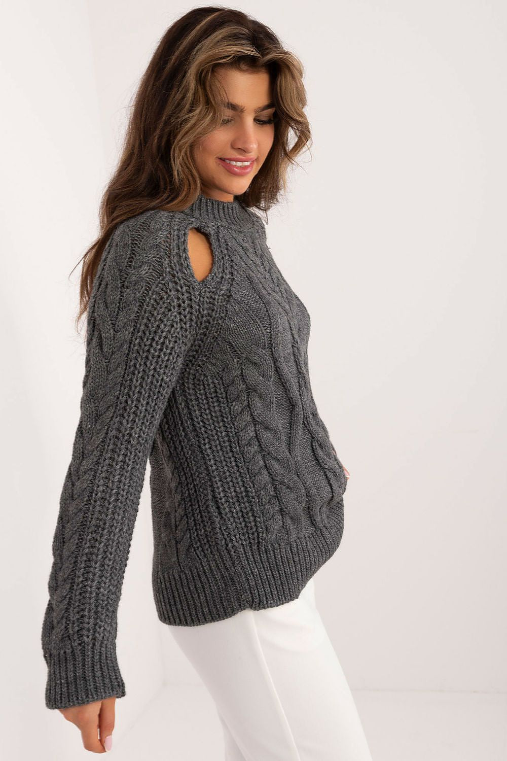 Woman wearing a gray cable knit sweater with cut-out design on a white background