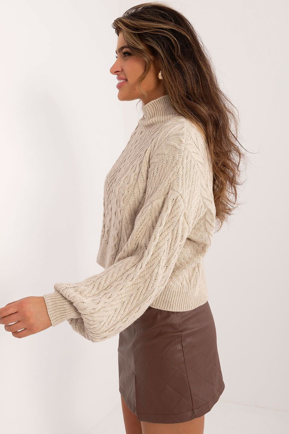 Woman wearing a beige cable knit sweater and brown leather skirt on a white background