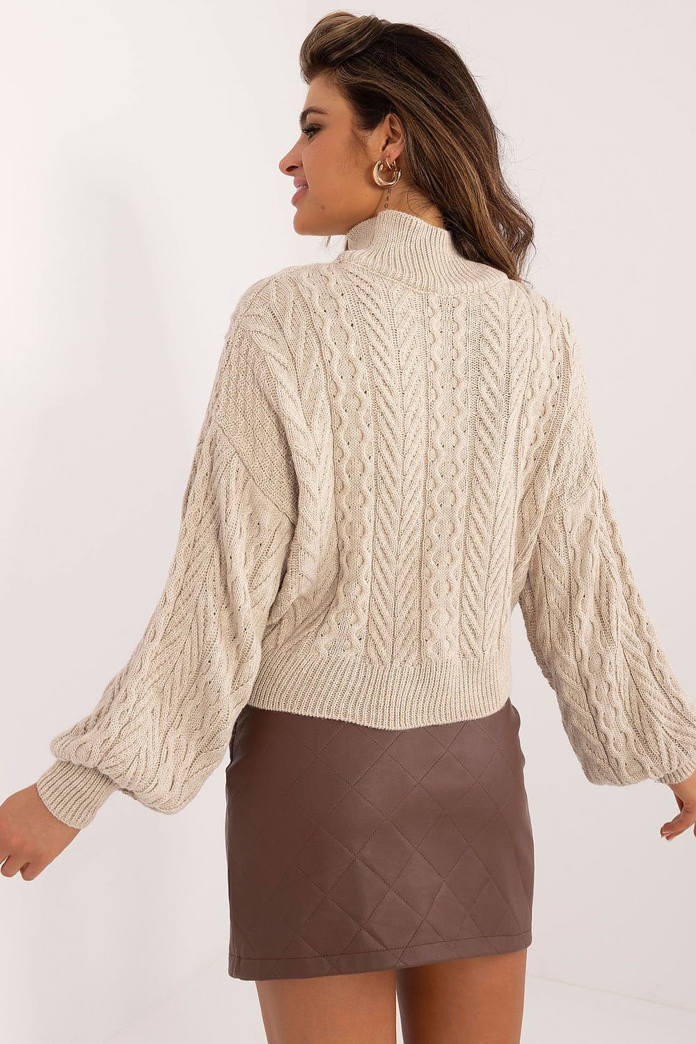 Woman wearing a beige cable knit sweater and brown skirt on a white background