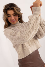 Woman wearing a beige cable knit sweater against a white background