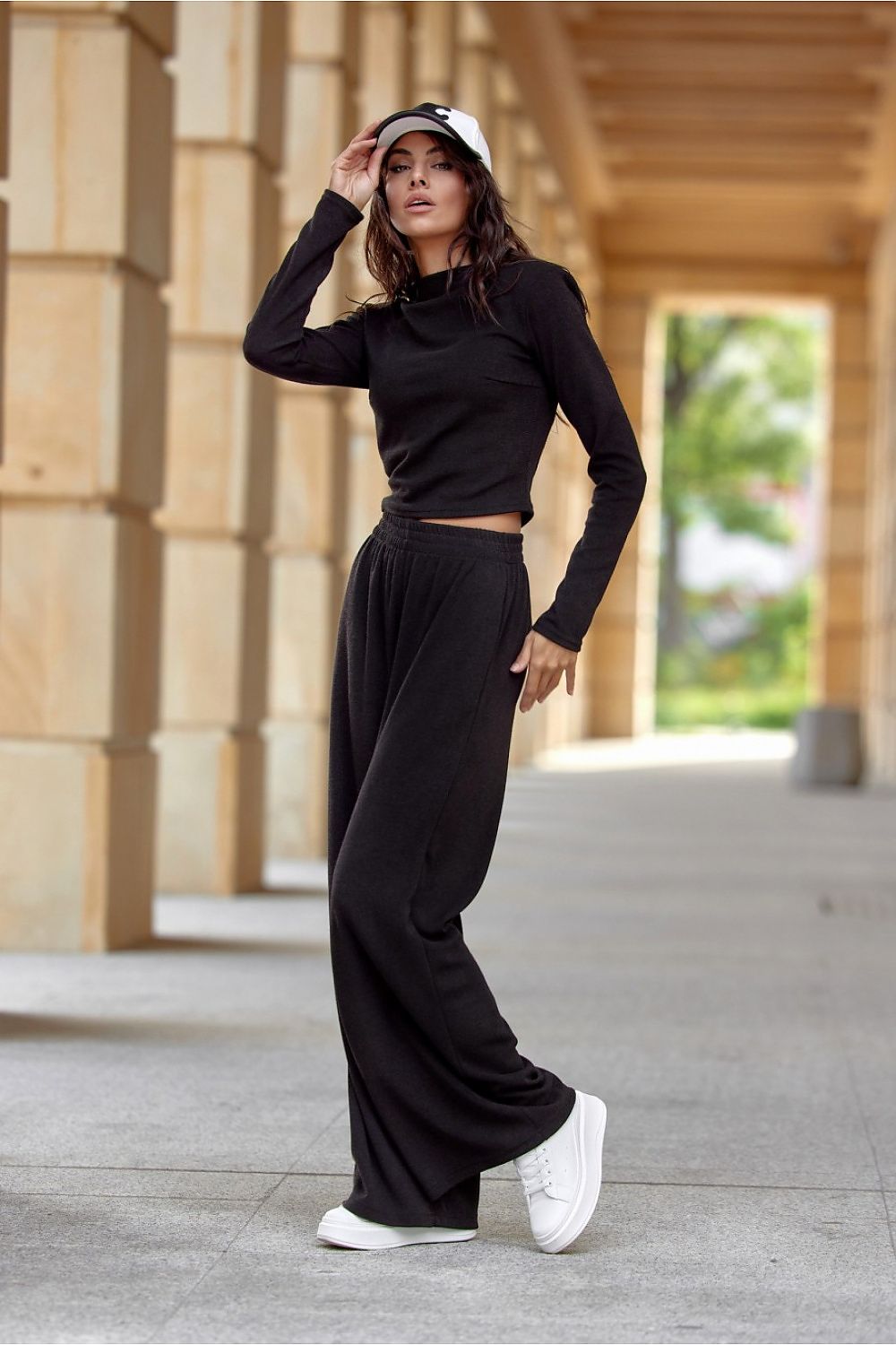 Woman in black outfit with white sneakers standing in an outdoor setting
