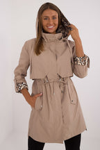 Woman wearing a beige trench coat with leopard print cuffs on a white background
