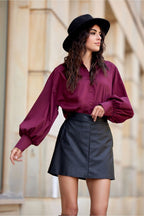 Woman wearing a purple blouse and black skirt with a blurred background