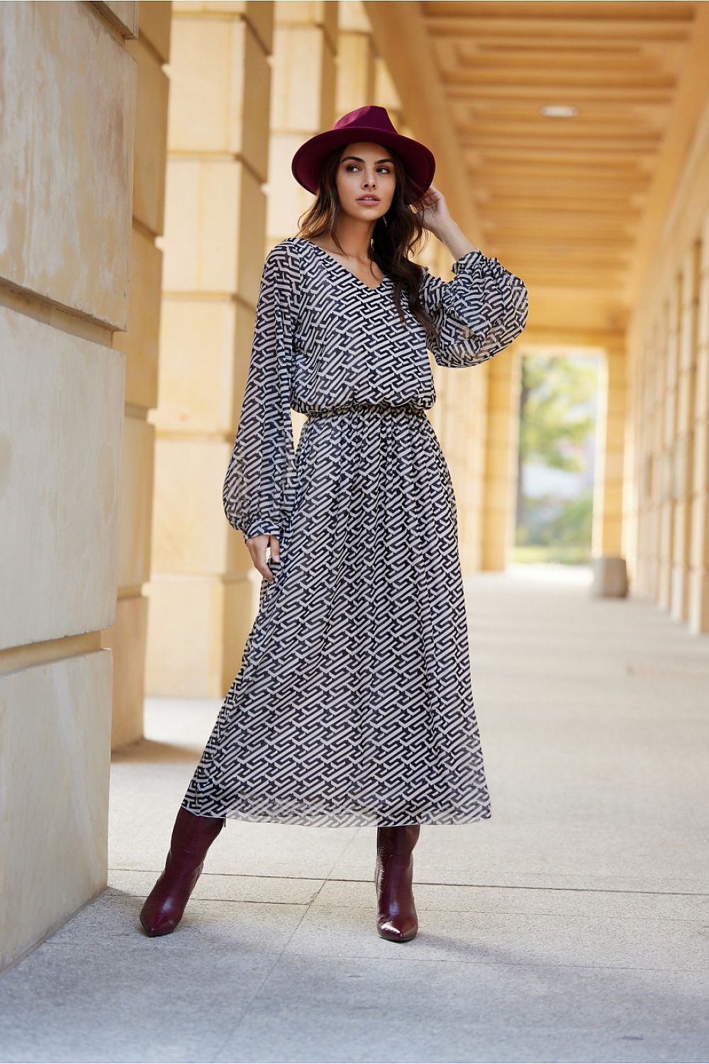 Woman in a patterned dress and red hat standing in an architectural setting