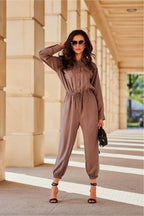 Woman in a brown jumpsuit standing on steps with a building in the background