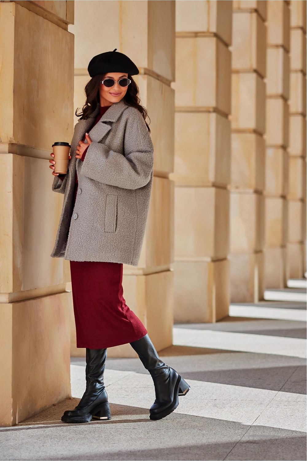 Woman in a gray coat and red skirt standing in front of a building