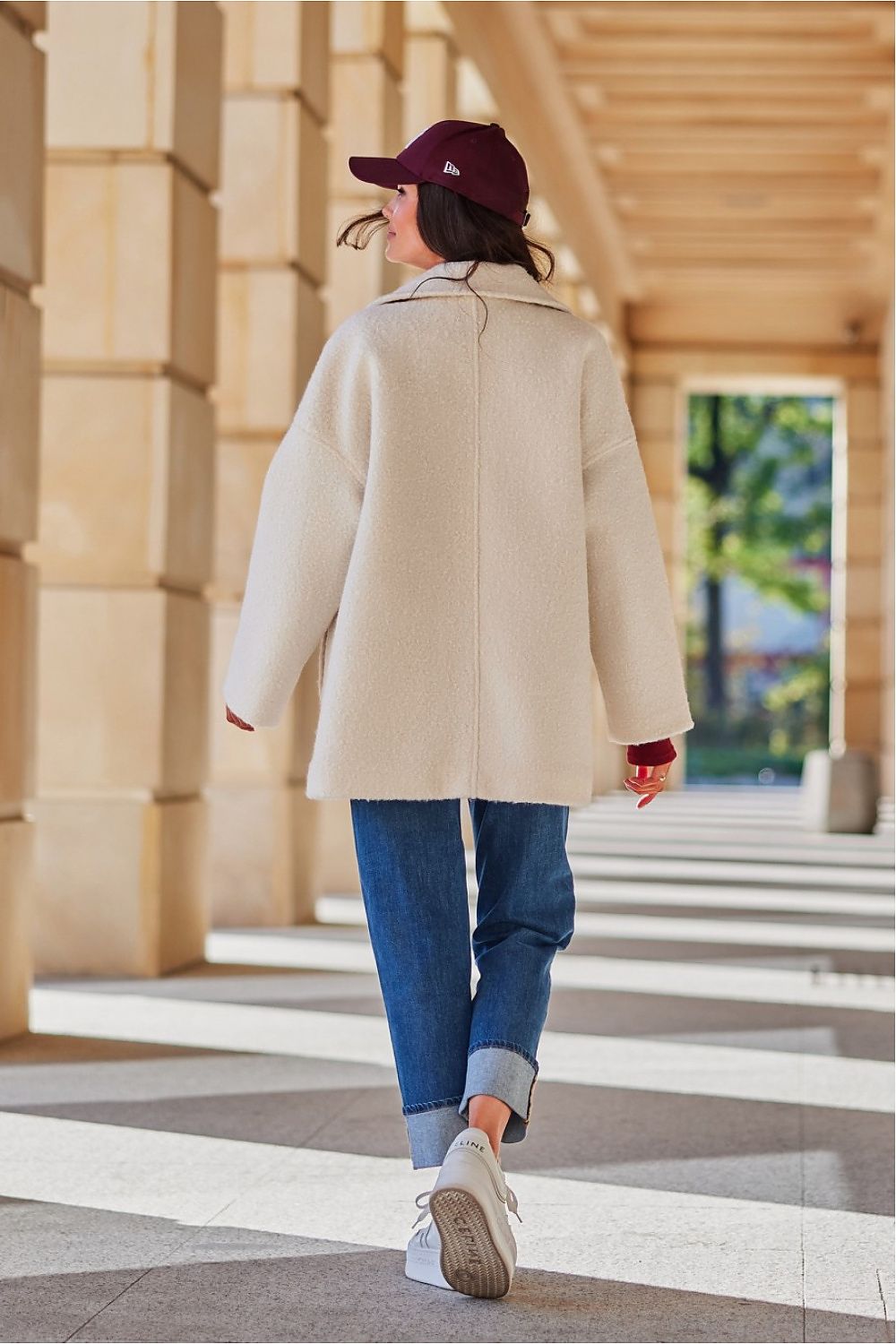 Person wearing a beige coat and blue jeans walking outdoors.