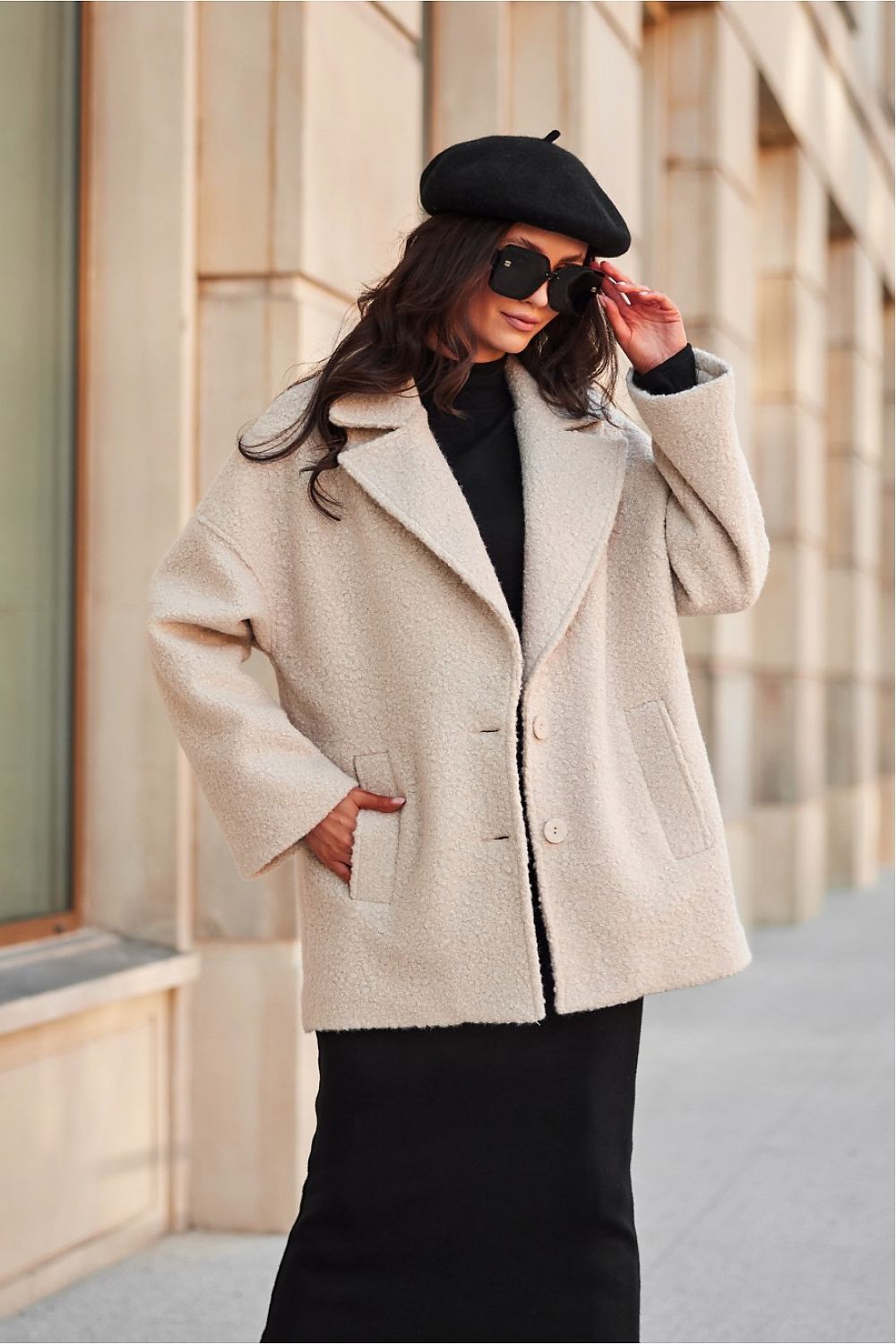 Woman wearing a beige coat, black beret, and sunglasses outdoors.