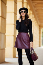 Woman wearing a black top, maroon leather skirt, and sunglasses with a blurred background