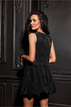 Woman wearing a black dress with a sequined top against a dark wall.