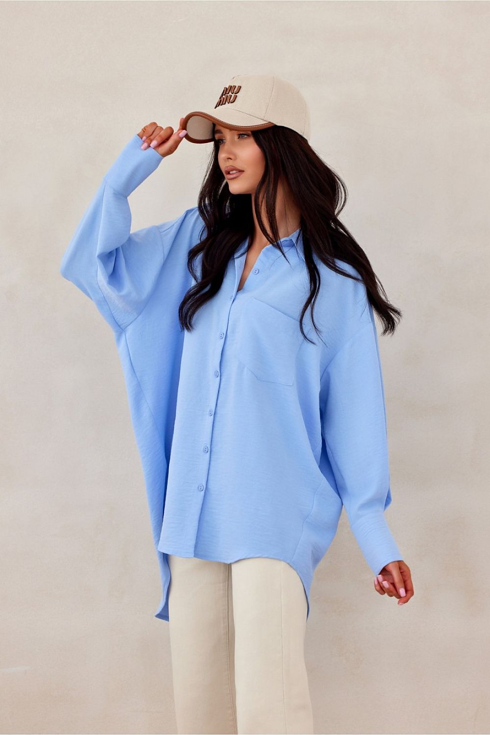 Woman wearing a light blue shirt and beige cap against a plain background