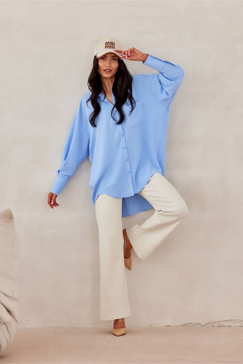 Woman wearing a light blue shirt and white pants against a beige background