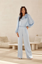 Woman in a light blue outfit standing in a minimalistic room with beige furniture.