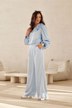 Woman wearing a light blue outfit with ruffled sleeves in a minimalistic room.