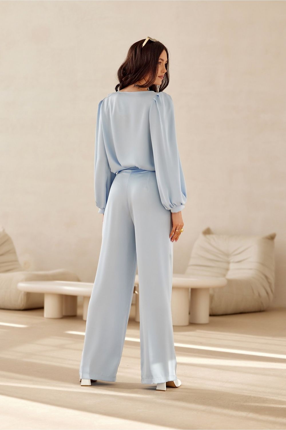 Woman in a light blue outfit standing in a minimalistic room with neutral decor.
