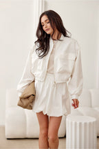Woman wearing a white outfit with a beige bag in a minimalistic room.