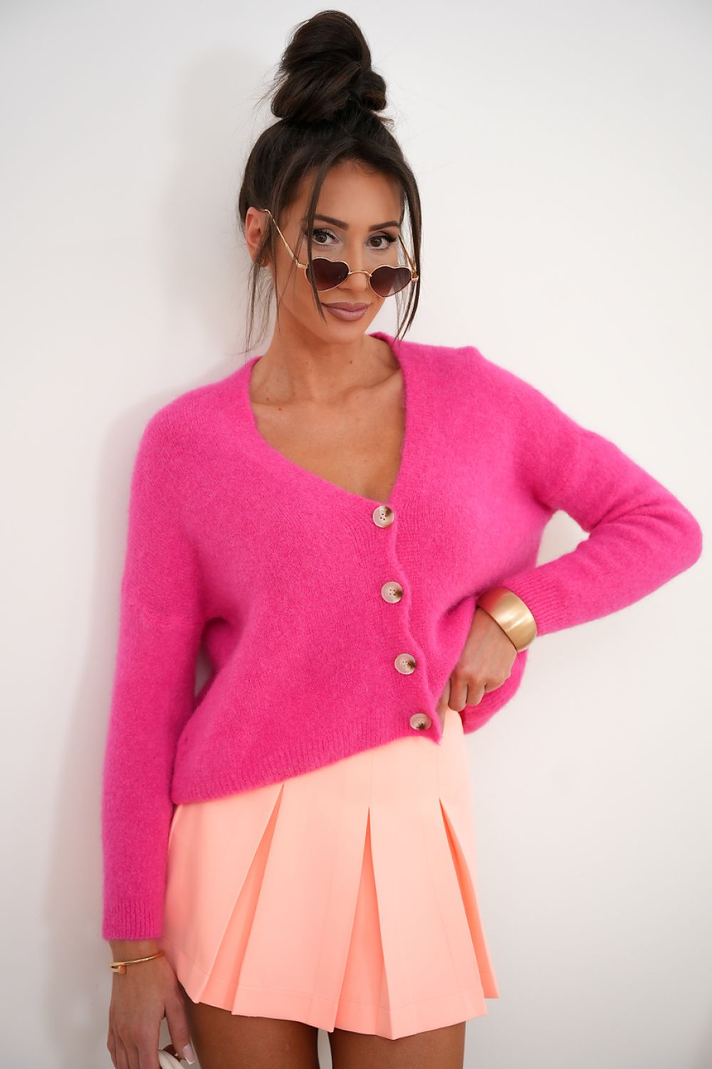 Woman wearing a bright pink cardigan and peach skirt against a white background