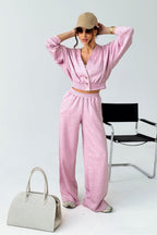 Woman in a pink outfit with a beige hat and handbag, standing next to a black chair on a white background.