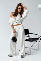 Woman in a white outfit posing against a gray background with a chair.