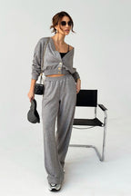 Woman in gray outfit standing next to a black chair on a white background