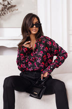 Woman wearing a black blouse with pink floral patterns, sitting on a white couch.