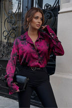 Woman wearing a pink floral blouse and black pants standing in front of an ornate black gate.