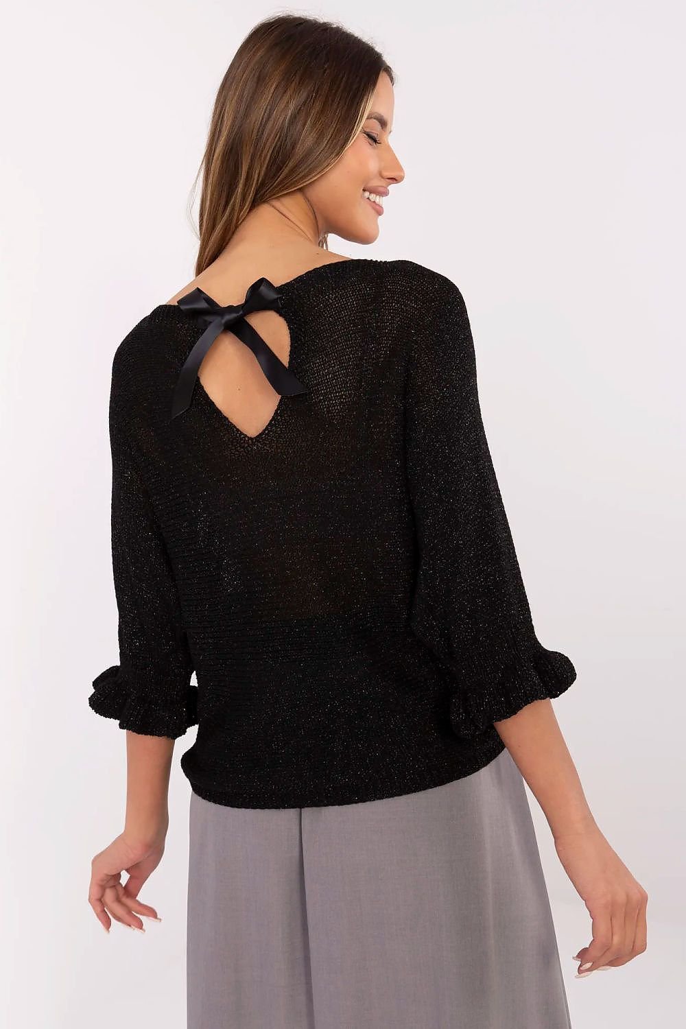 Woman wearing a black sweater with a bow detail on the back against a white background
