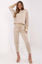 Woman wearing a beige lounge set with gold accents on a white background