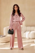 Woman in a pink outfit holding a black handbag in a living room setting.