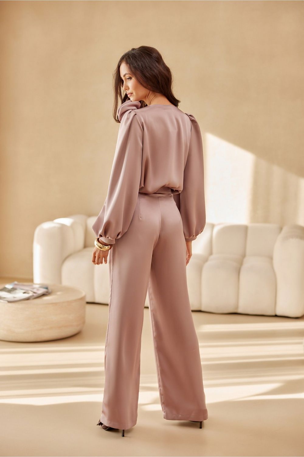 Woman in a pink outfit standing in a stylish room with beige walls and furniture.