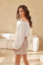 Woman wearing a light-colored off-shoulder top and beige skirt in a softly lit room.